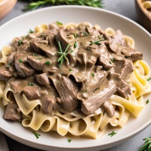 A bowl of beef stroganoff served over egg noodles, topped with fresh rosemary.