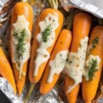 Campfire carrots in an open foil packet, topped with melted cheese and fresh herbs, ready to be served (1)